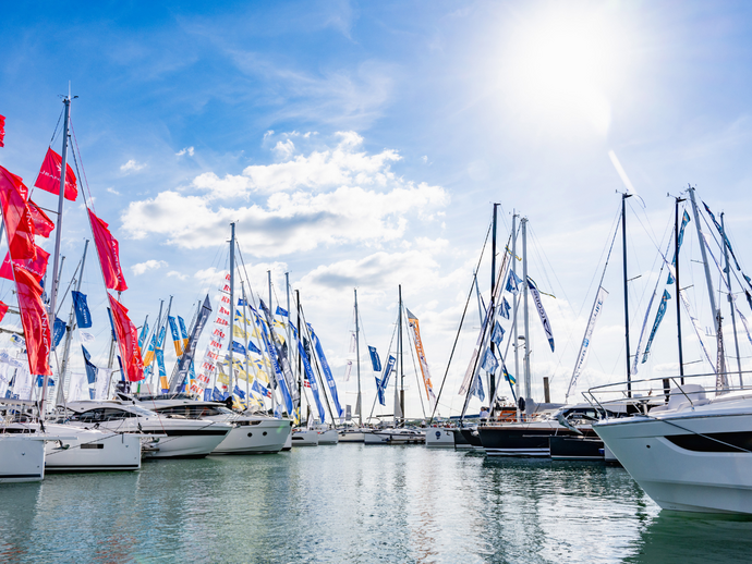 Several sailboats with colorful flags docked at a marina under a bright sky with sun and scattered clouds.