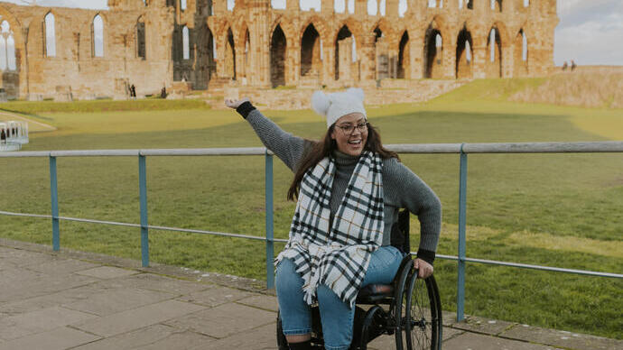A woman in a wheelchair in front of a ruined abbey.