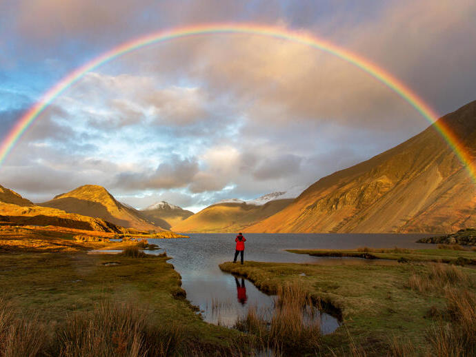 Man standing on the edge of a lake watching a rainbow