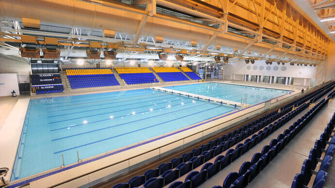 Grande piscina coperta con tribune blu e gialle, ben illuminata.