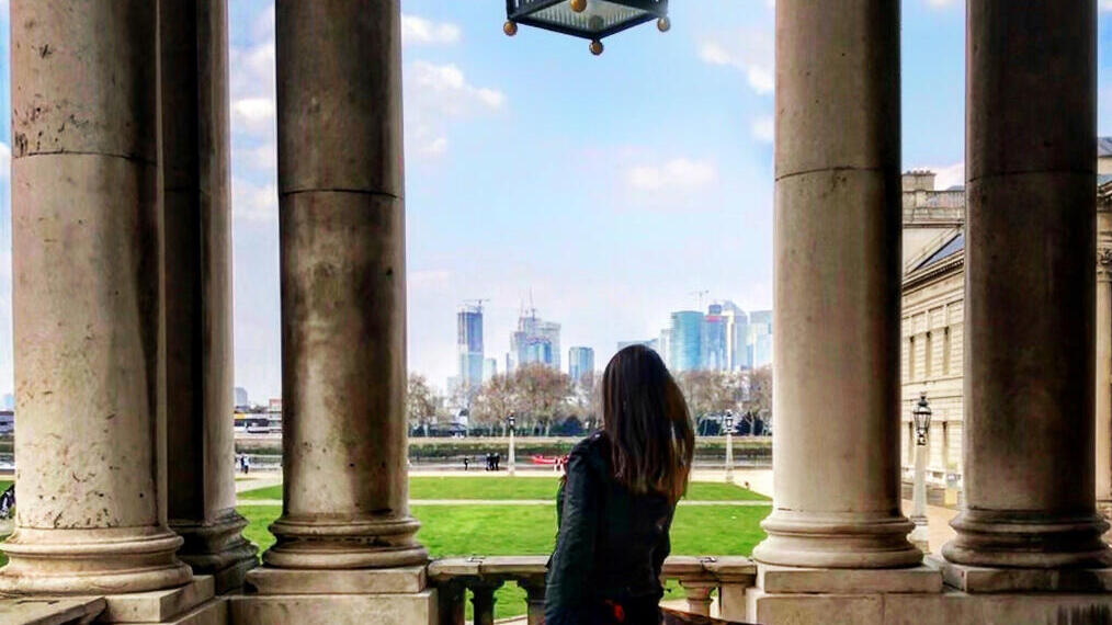 Femme debout sous une grande lanterne en verre, regardant à travers les colonnades vers les bâtiments modernes de la ville