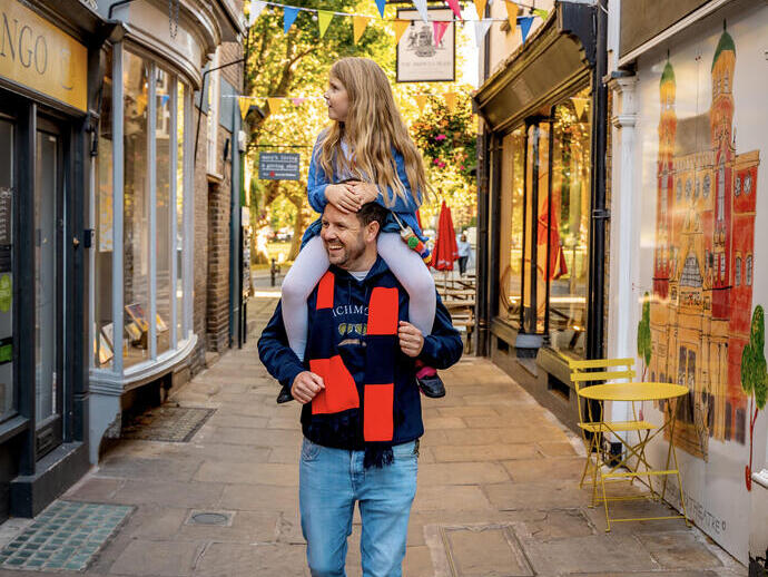 Un hombre con un niño a hombros camina por una calle peatonal con tiendas a ambos lados