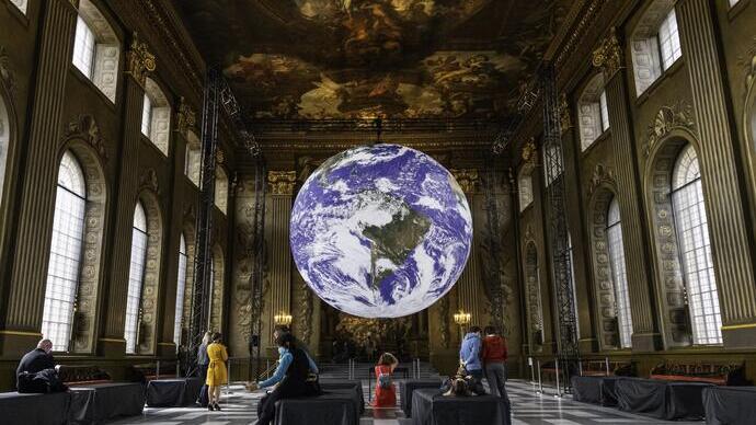 Persone in una grande sala in cui una scultura del pianeta Terra illuminato è appesa al soffitto