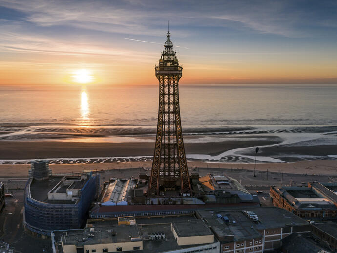 Tall tower on the side of the beach with the sun setting over the sea
