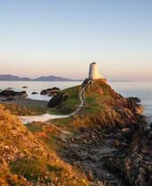 A path leading to a lighthouse on a prominent rocky outcrop by the sea