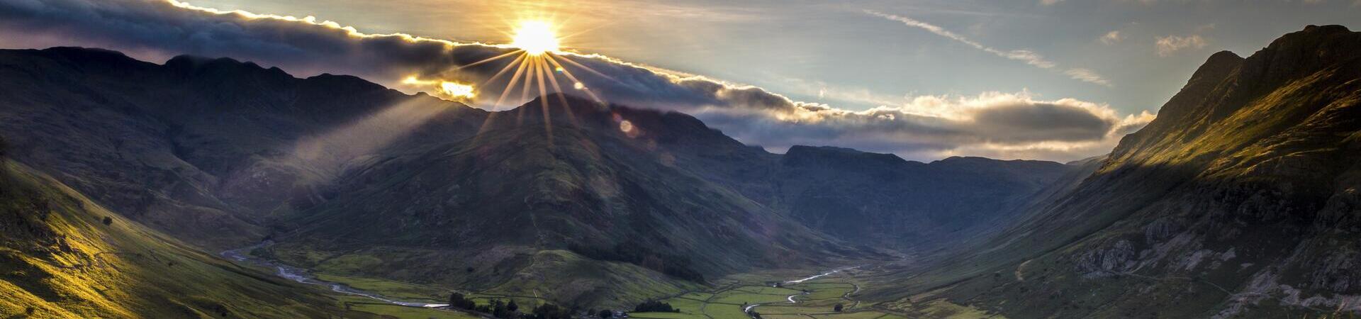 Man sitting in long grass on the side of a fell watching the sunset