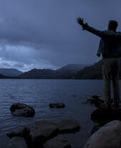 Silhouette d'un homme debout, les bras tendus, sur le rivage