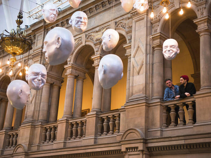 Two men looking at installation of suspended head sculptures inside a museum.