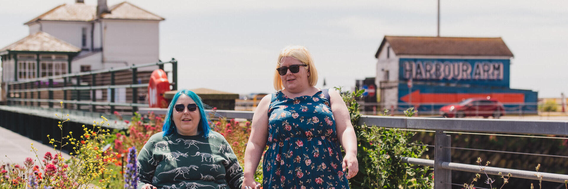 A woman walks with another women who sits in a wheelchair at an old railway station