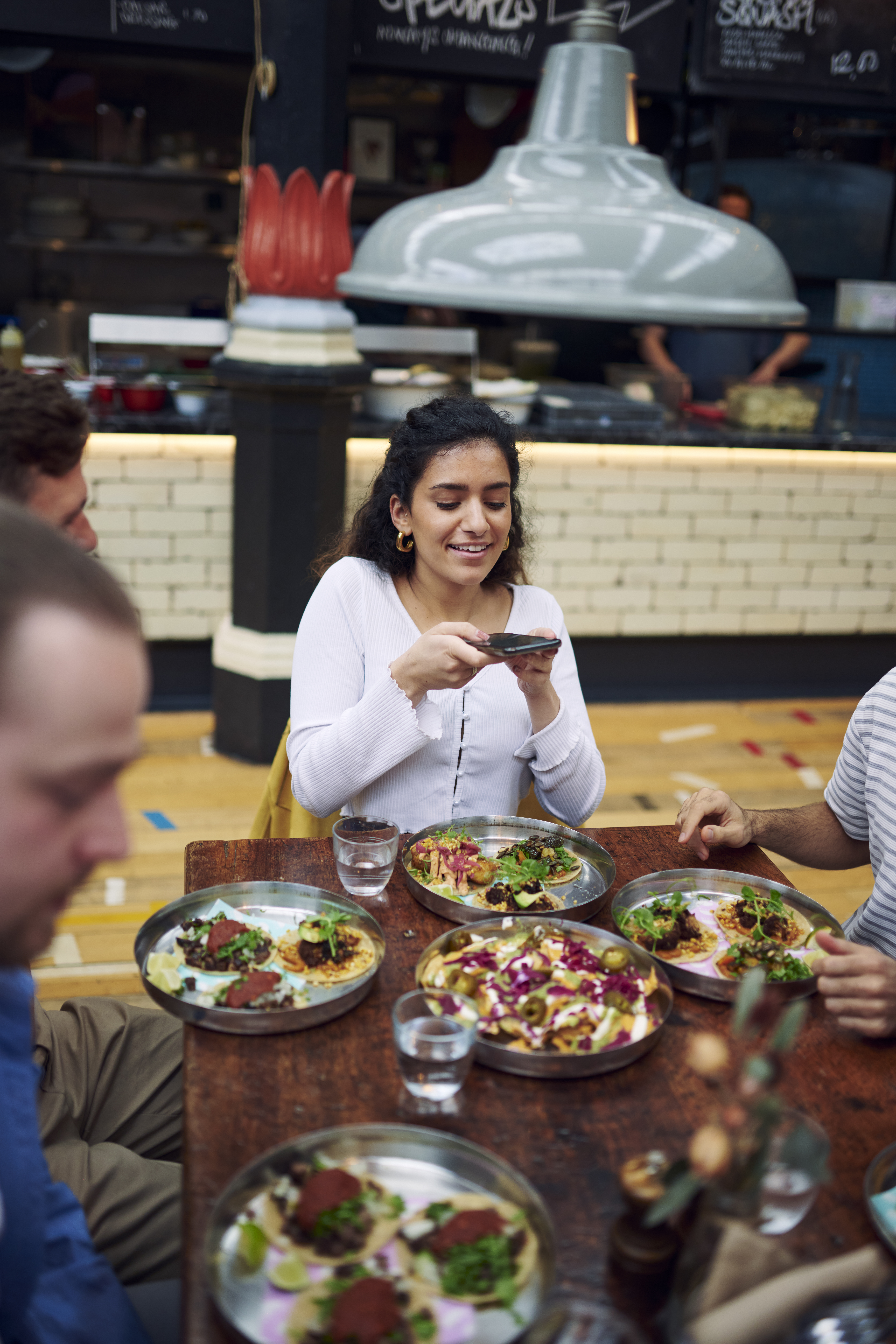 Frau, die mit Freunden an einem Tisch sitzt und ein Foto von Speisen in einem Food Court macht