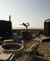 Woman holds a yoga pose standing on the edge of small plunge pool on the beach