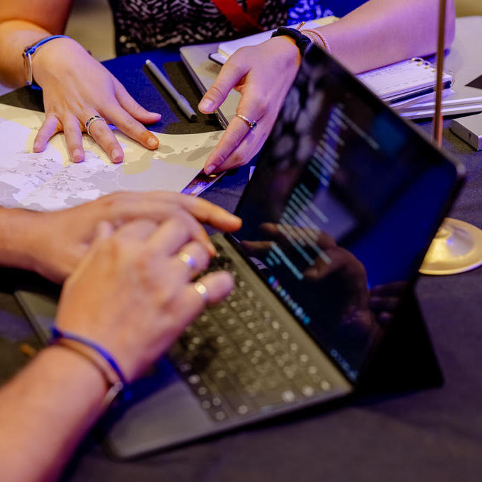 Two people work together at a table with a laptop, map, notebooks, and business cards, suggesting a collaborative or planning meeting.
