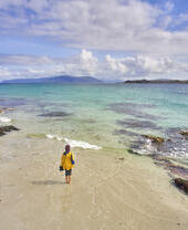 A young woman walking on the white sand with the crystal clear blue waters of a shallow beach area.