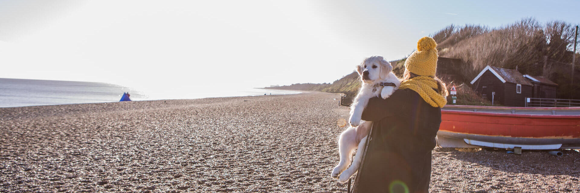 A woman carrying a dog along a beach in Dunwich