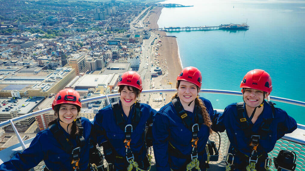 Group of friends in climbing gear at the top of i360 pod overlooking the Brighton coastline. in Brighton