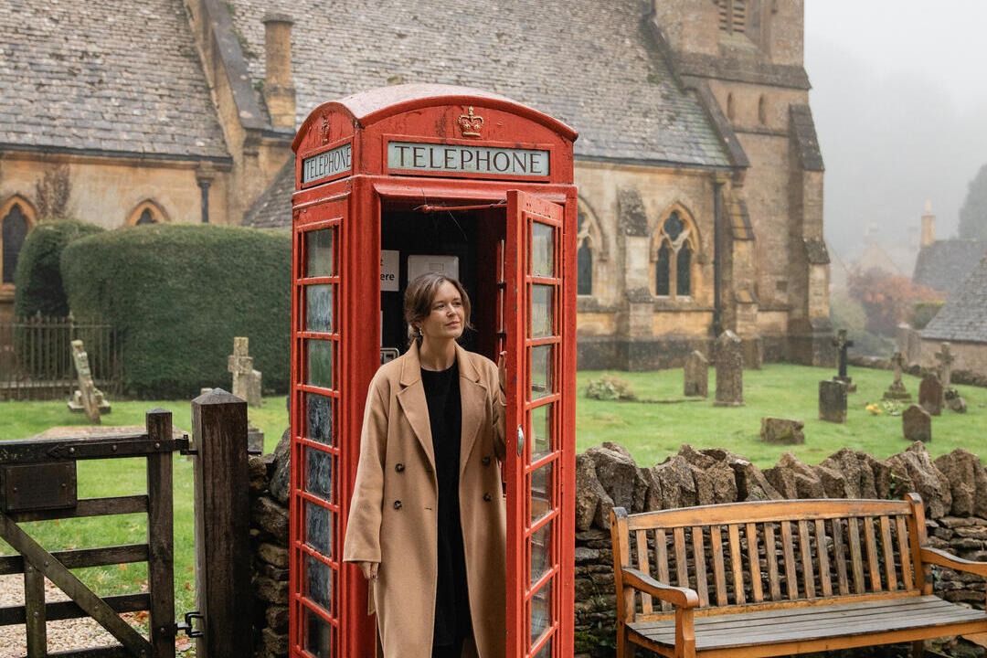 A woman exits a red telephone box with a church in the background