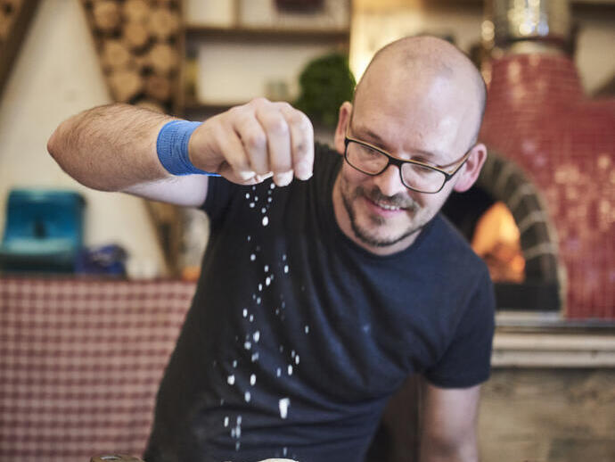 Mann, der auf einem Lebensmittelmarkt Käse auf Pizza streut