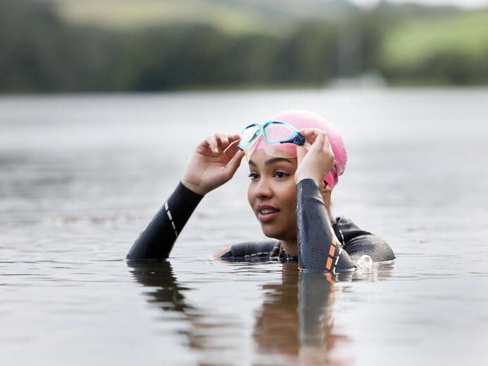 A woman in a wetsuit and goggles swimming in a large lake.