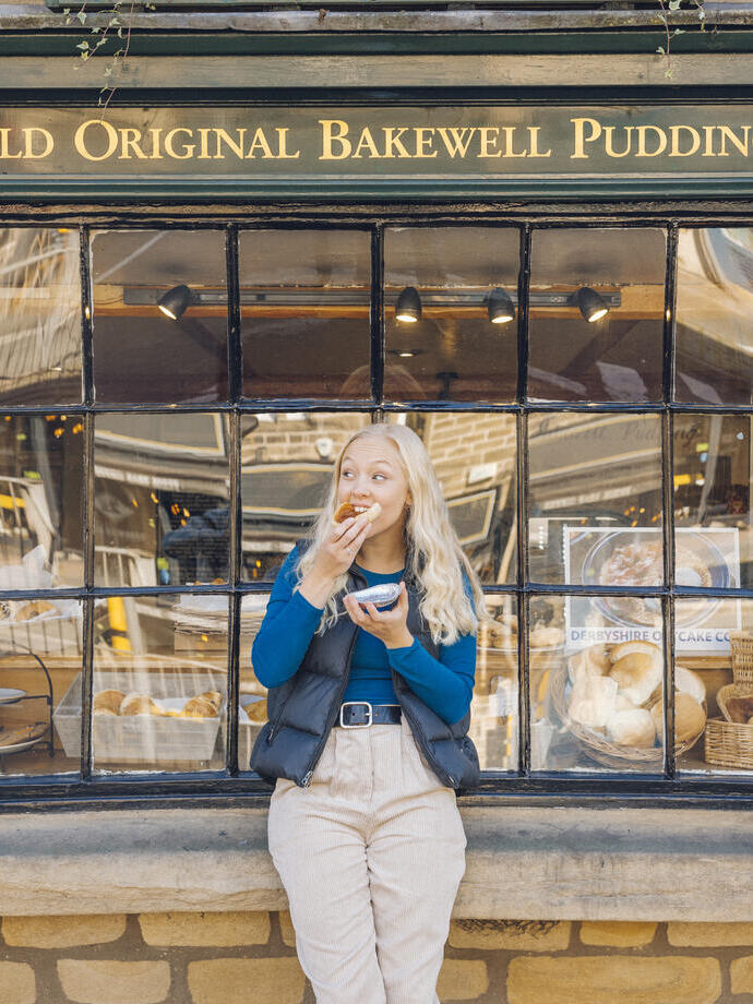 Woman eating bakewell tart in front of bakery