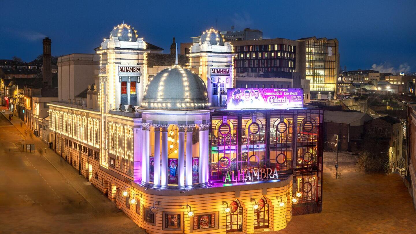 Night view of the illuminated Alhambra Theatre with bright lights and classical architecture on a city street.