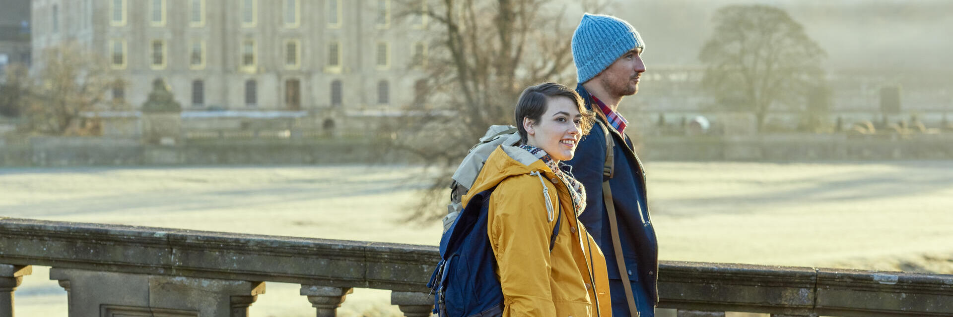 Couple walking on a stone bridge, a large country house in the backround