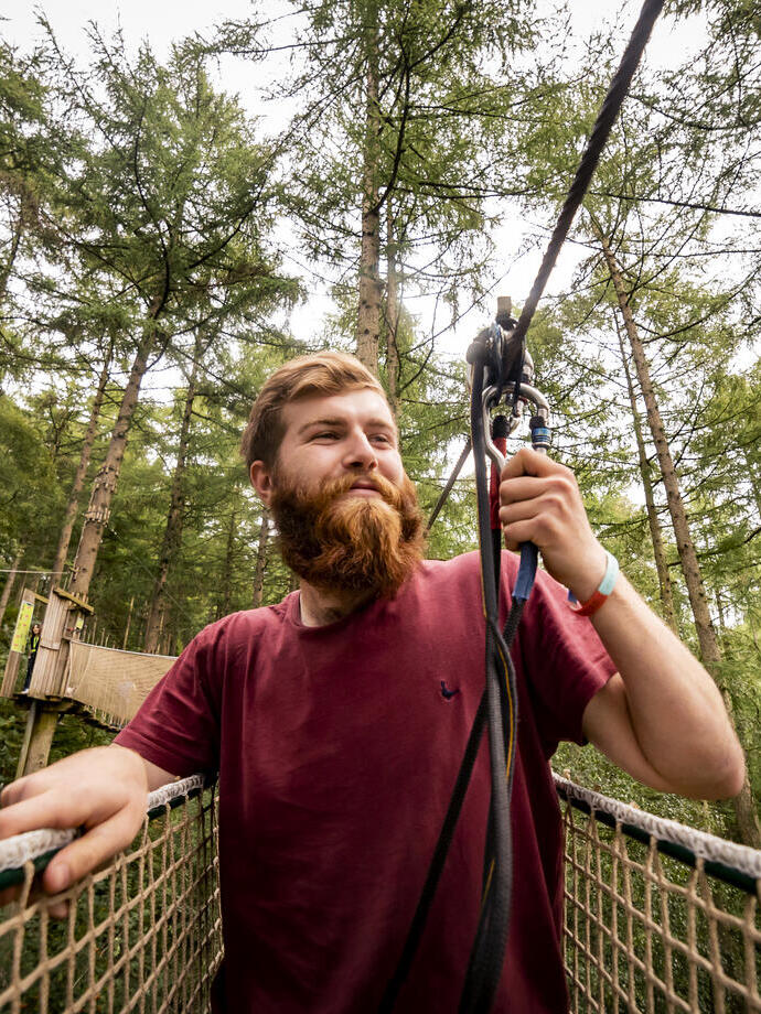 Mann, der an einem Sicherheitsseil befestigt ist – Go Ape Dalby Forest