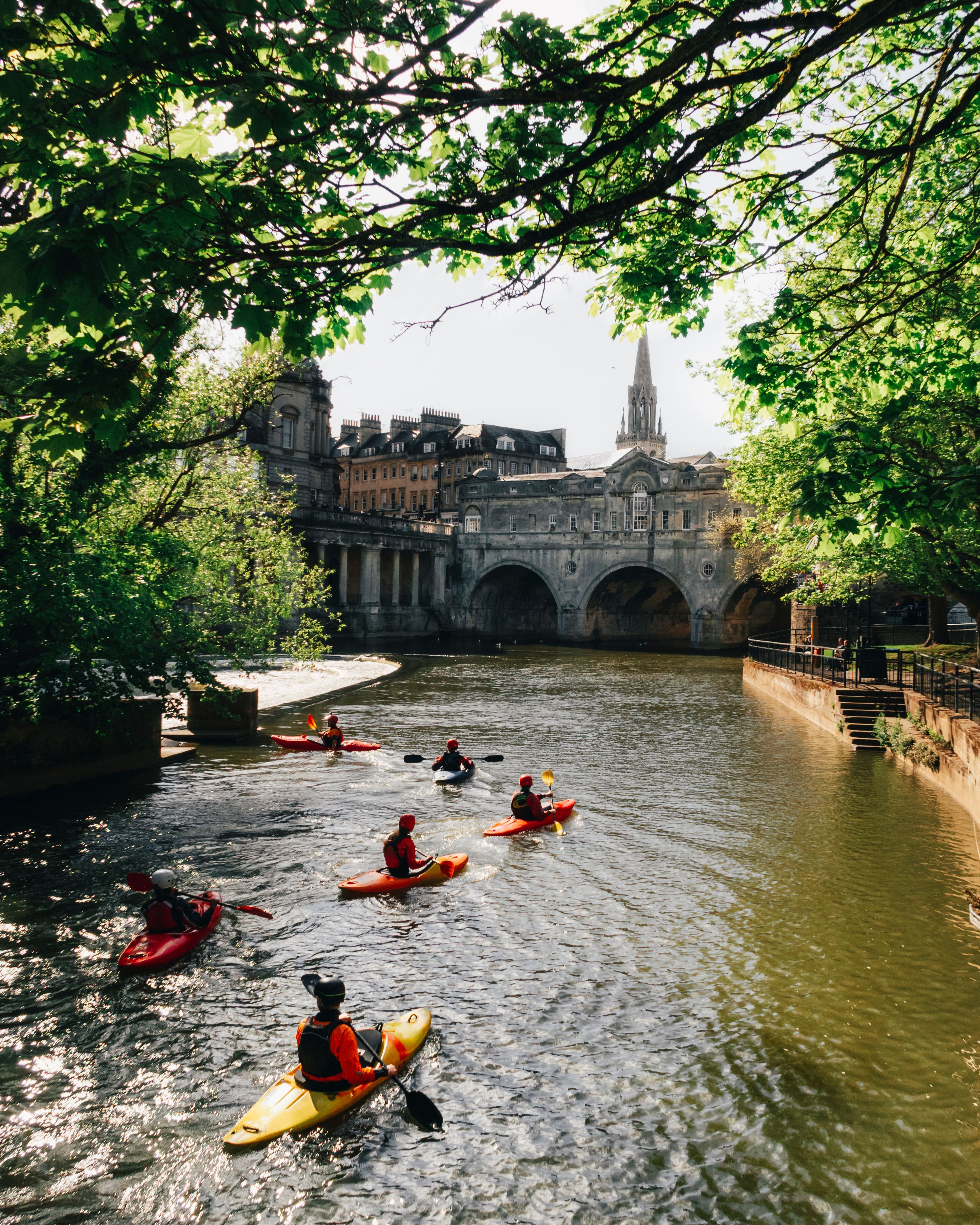 Group of people kayaking on the river by a bridge in a city