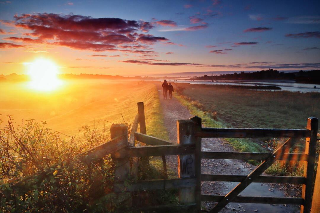 Two people walking along trail at sunset with gate in the foreground