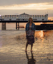Woman standing on the beach near the pier at sunset