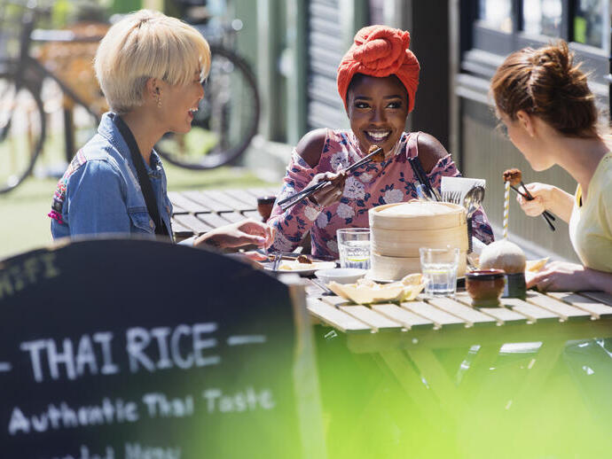 Tres jóvenes amigas disfrutando de un almuerzo de dim sum en una soleada cafetería con terraza