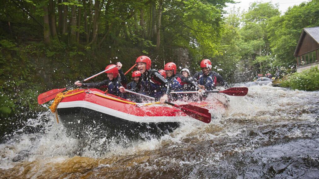 People wearing wetsuits and helmets paddling down a rapid