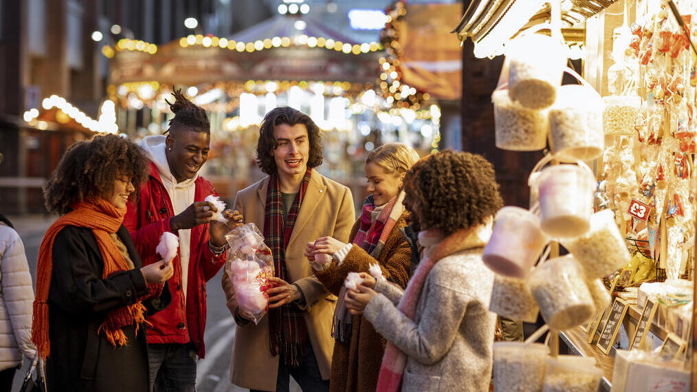 Gruppe junger Freunde, die sich auf dem Weihnachtsmarkt eine Tüte Zuckerwatte teilen.