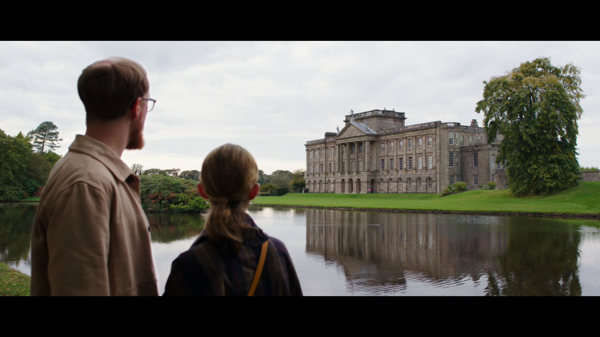 Un uomo e una donna in piedi su un lago guardano verso una casa storica