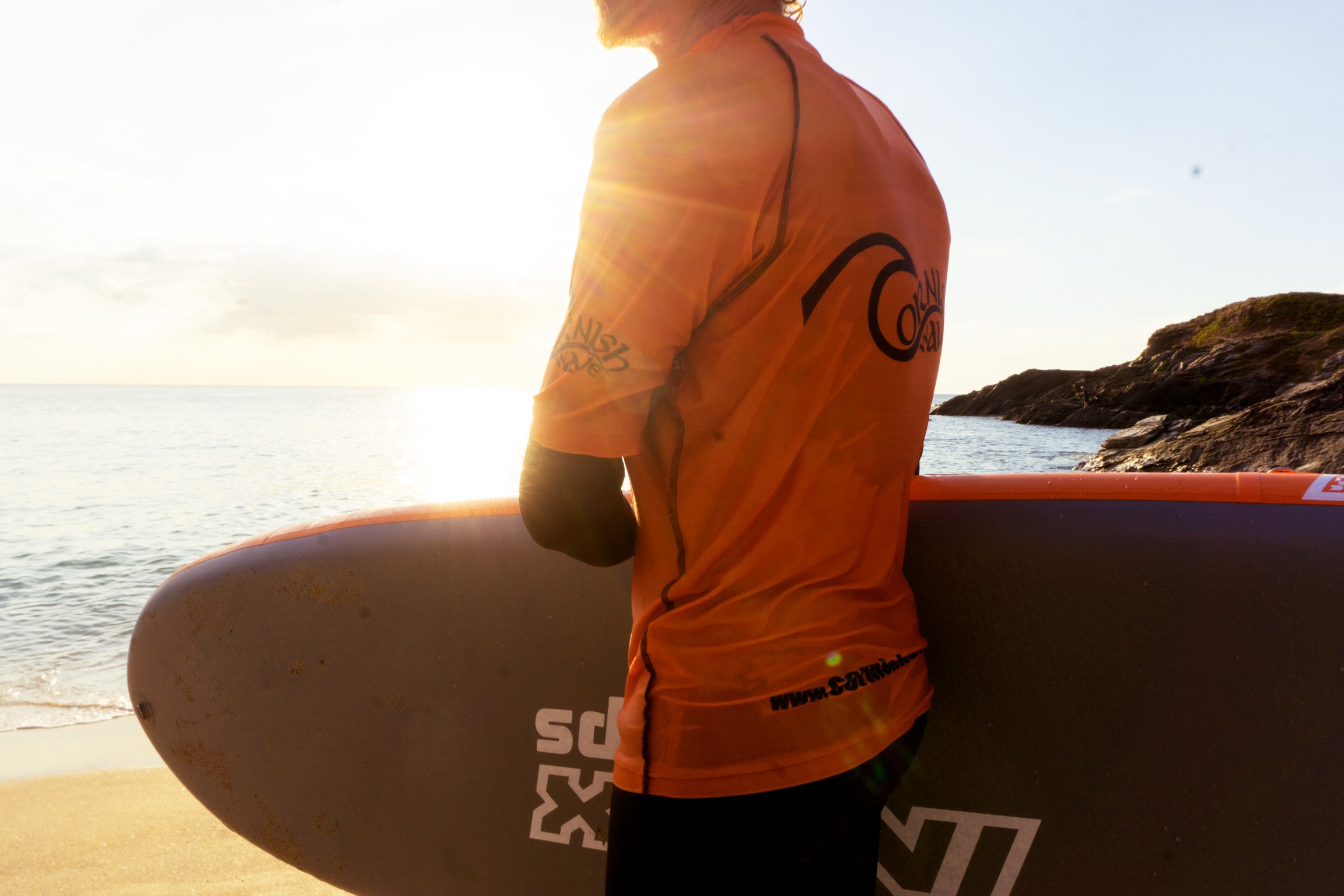 Ein Mann mit einem Surfbrett an einem Strand in Cornwall