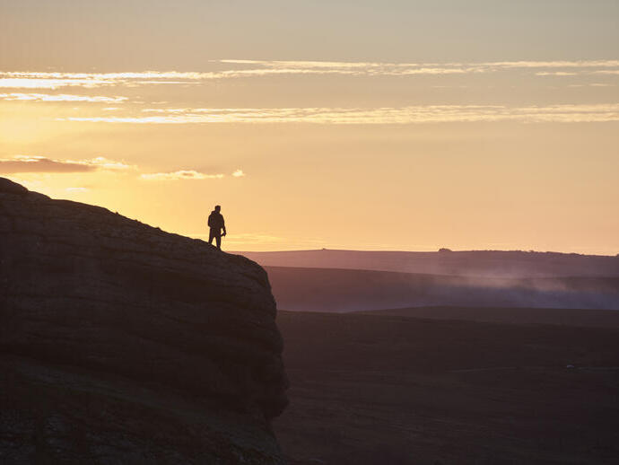 Silhouette d'une personne faisant une randonnée sur une grande colline au coucher du soleil
