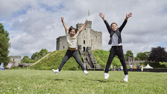 Two children jumping in front of a castle.