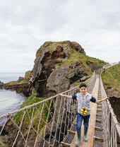 Child crossing a long rope bridge over the cliffs by the sea