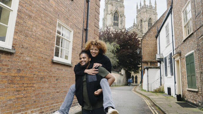 Ein Mann trägt eine Frau Huckepack in einer Stadtstraße mit einer Kathedrale im Hintergrund