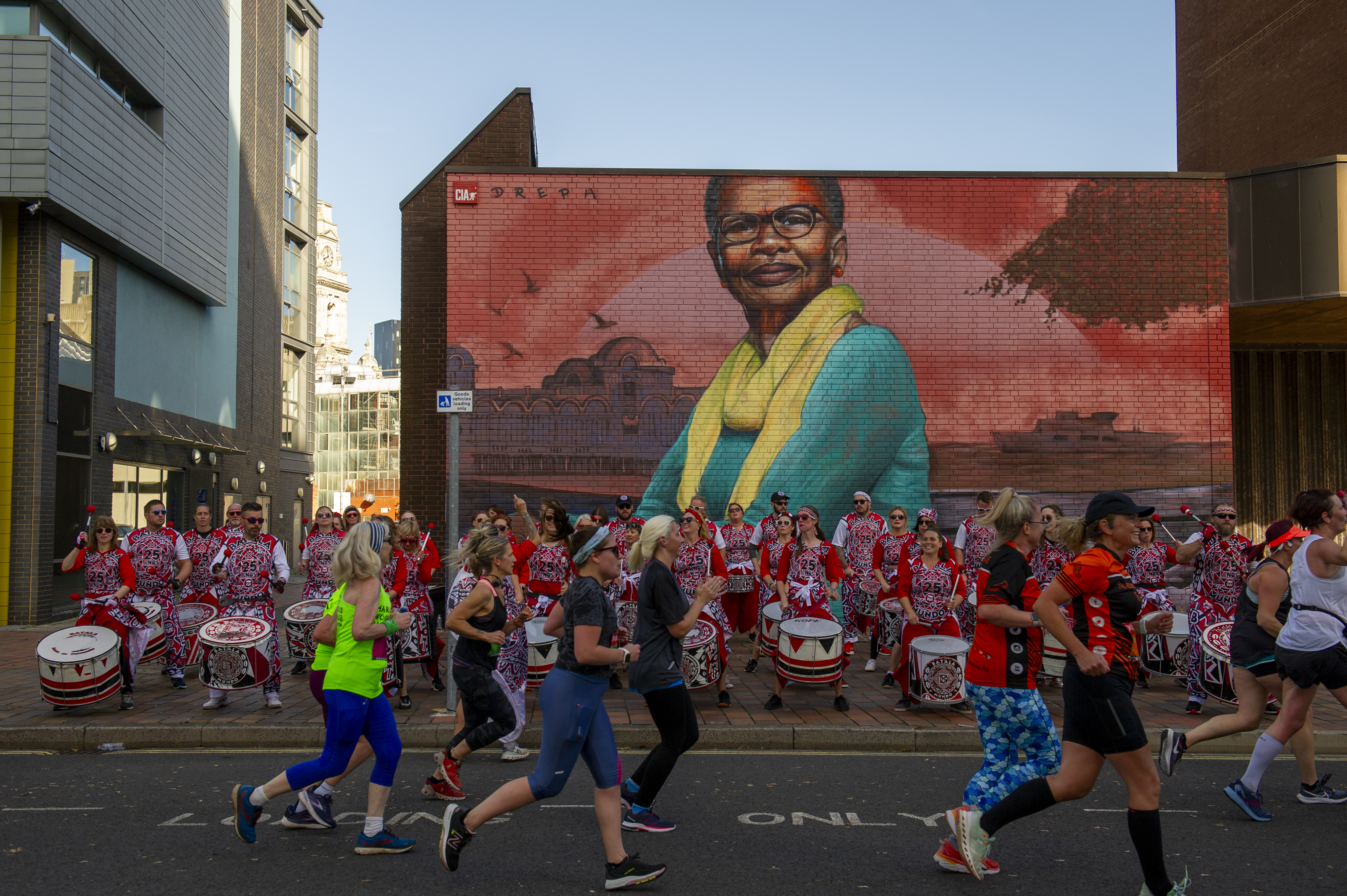 People running in front of a drumming band and colourful street art