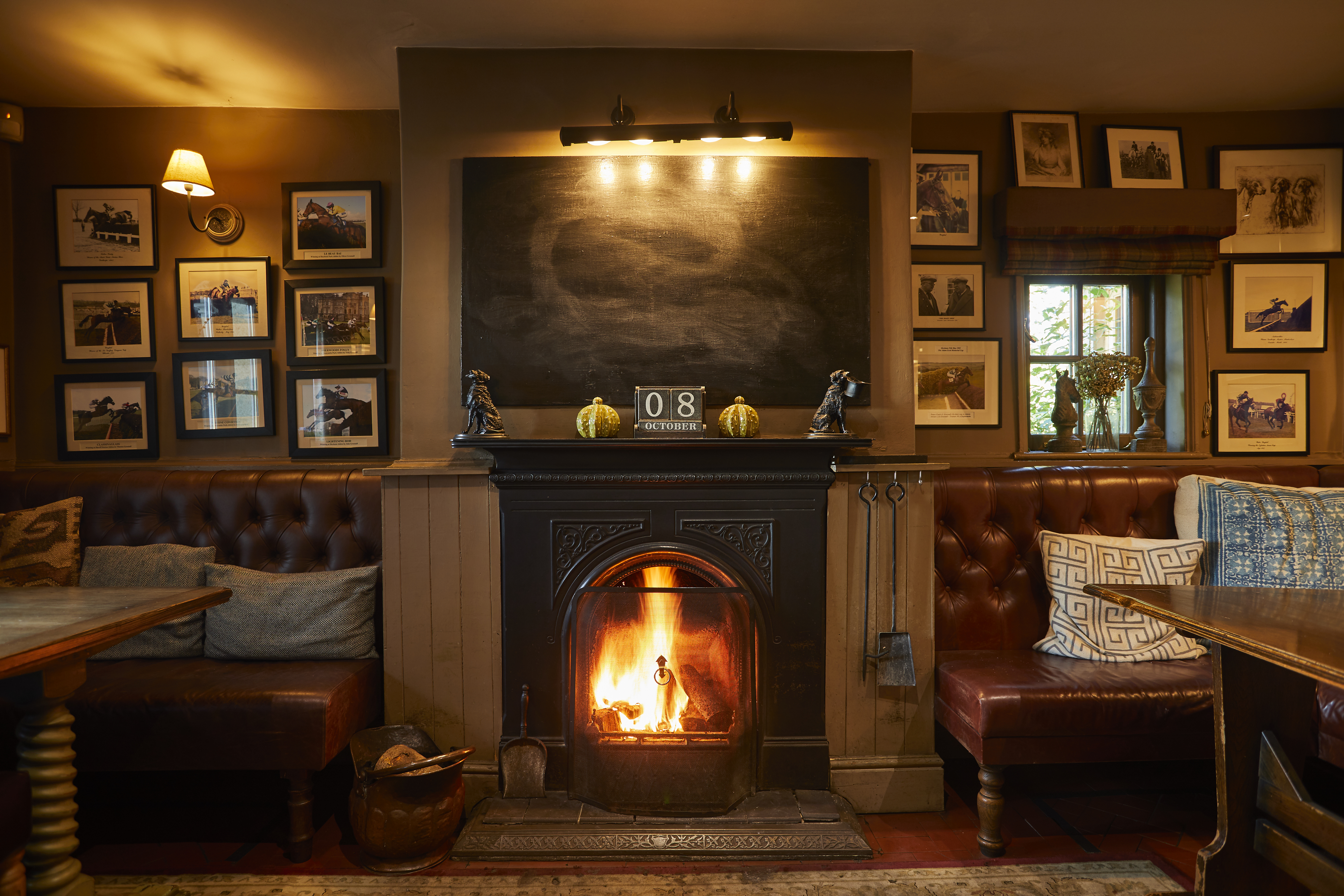 A fireplace in a pub with a lit fire flanked by two leather sofas with tables