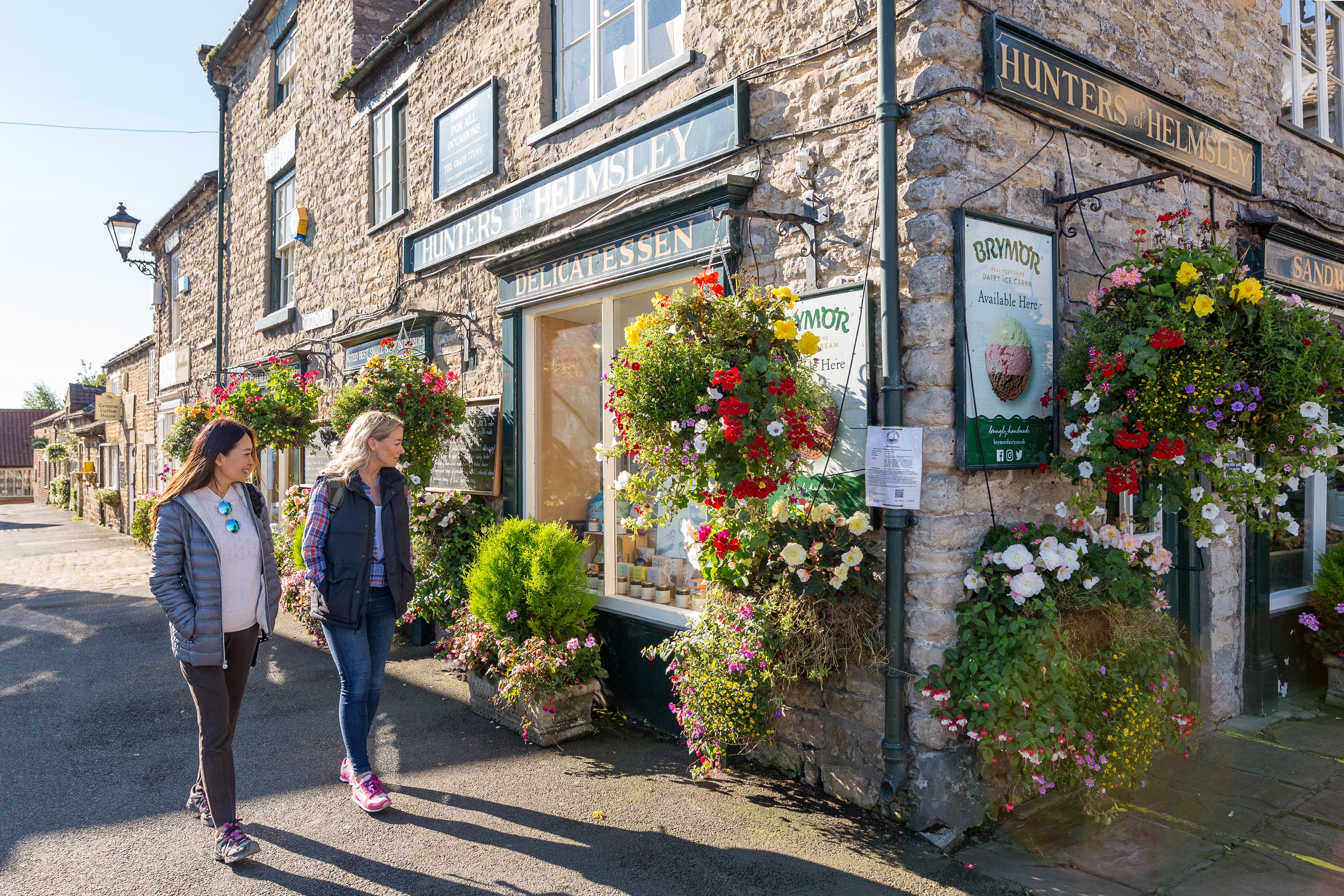 Two women walking past a shop in a village