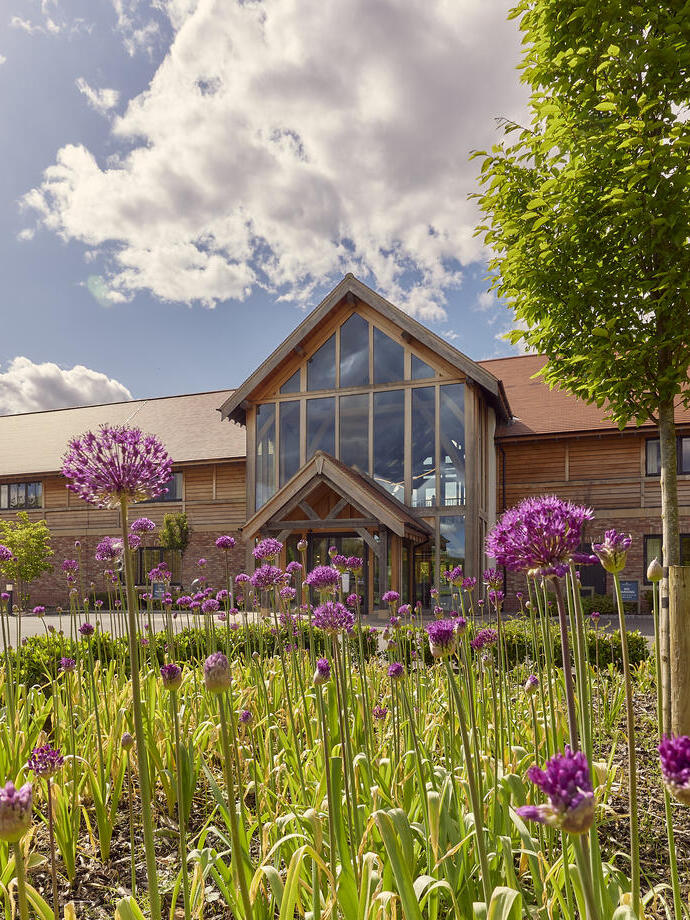 The external frontage of one of the hotel buildings with grass and flowers in the sunshine at a luxury golfing grounds and accommodation venue.