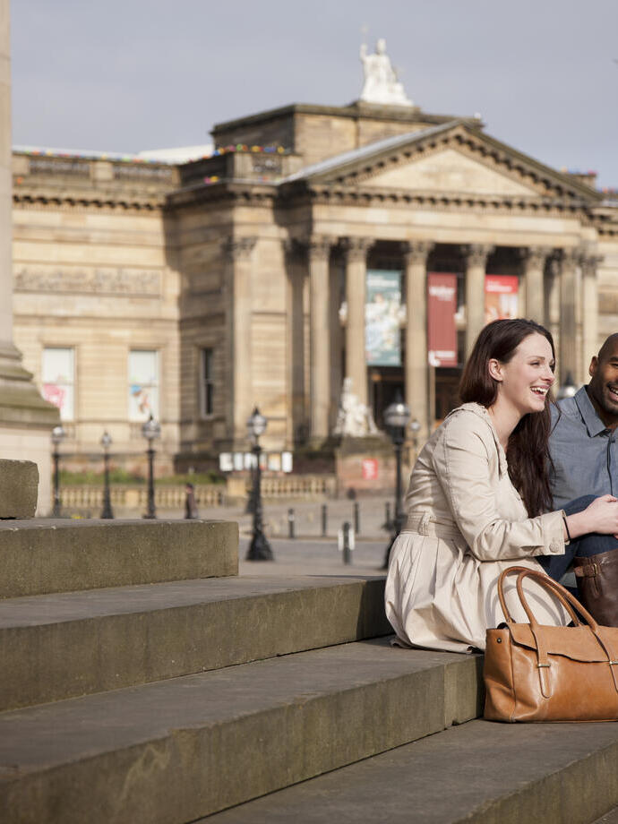 Liverpool city centre. Lime Street. Two people, a couple, sitting on the steps outside St George's Hall in front of the Walker Art Gallery, in Liverpool.