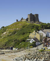 A castle on top of a hill beside a beach, surrounded by colourful buildings.