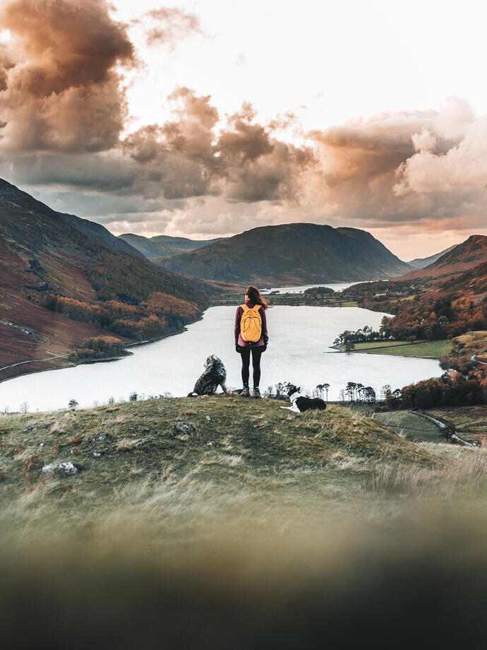 Woman standing with two dogs looking down at a lake in a valley