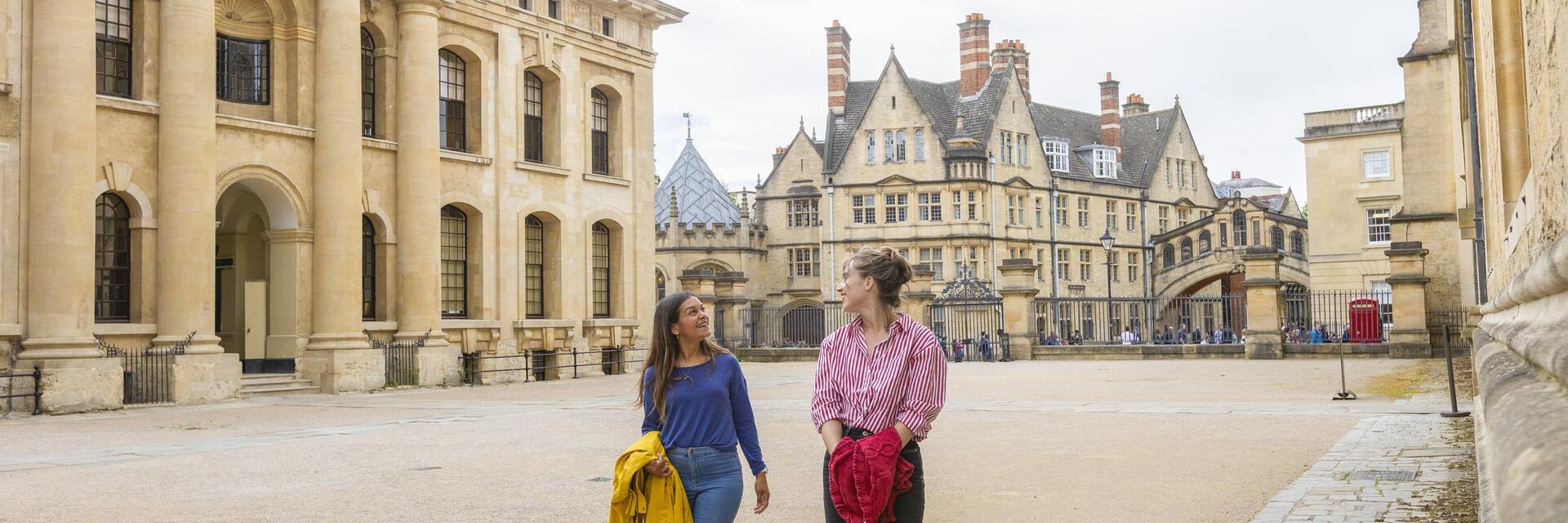 Two women walk across a courtyard among heritage buildings
