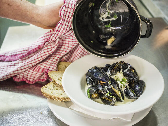 A chef plating up a bowl of mussels in a restaurant.