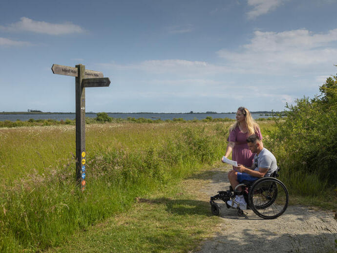 A man who uses a wheelchair and a woman review a map in the countryside