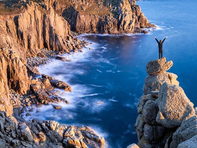 Mann, der auf einem felsigen Gipfel am Rande der Küste steht und über die Landzunge blickt