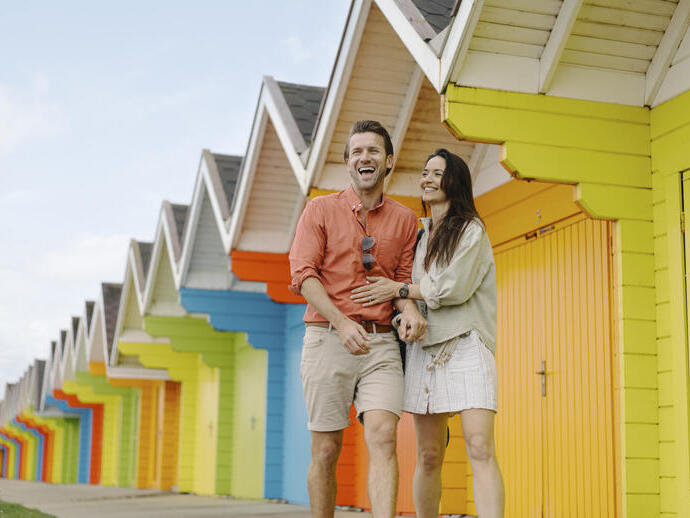 A man and woman laughing outside colourful beach huts